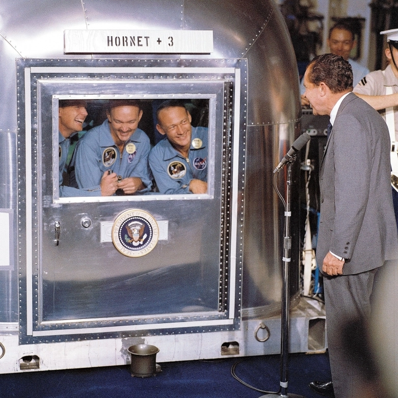 24 lipca 1969 roku – prezydent USA Richard M. Nixon wita astronautów Apollo 11 na pokładzie statku ratowniczego USS Hornet. W mobilnym obiekcie kwarantanny (czyli przerobionej przyczepie Airstream) od lewej: dowódca misji Neil A. Armstrong, pilot Michael Collins oraz Edwin E. Aldrin Jr. Kwarantannie poddani zostali wszyscy trzej, pomimo tego że tylko astronauci Armstrong i Aldrin zeszli na Księżyc, Collins pozostał na orbicie księżycowej - zdjęcie 11